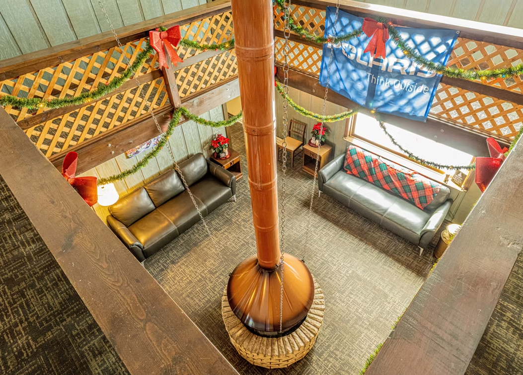 Rustic indoor lounge with woven walls, central wooden pole, and two metal sofas with colorful cushions