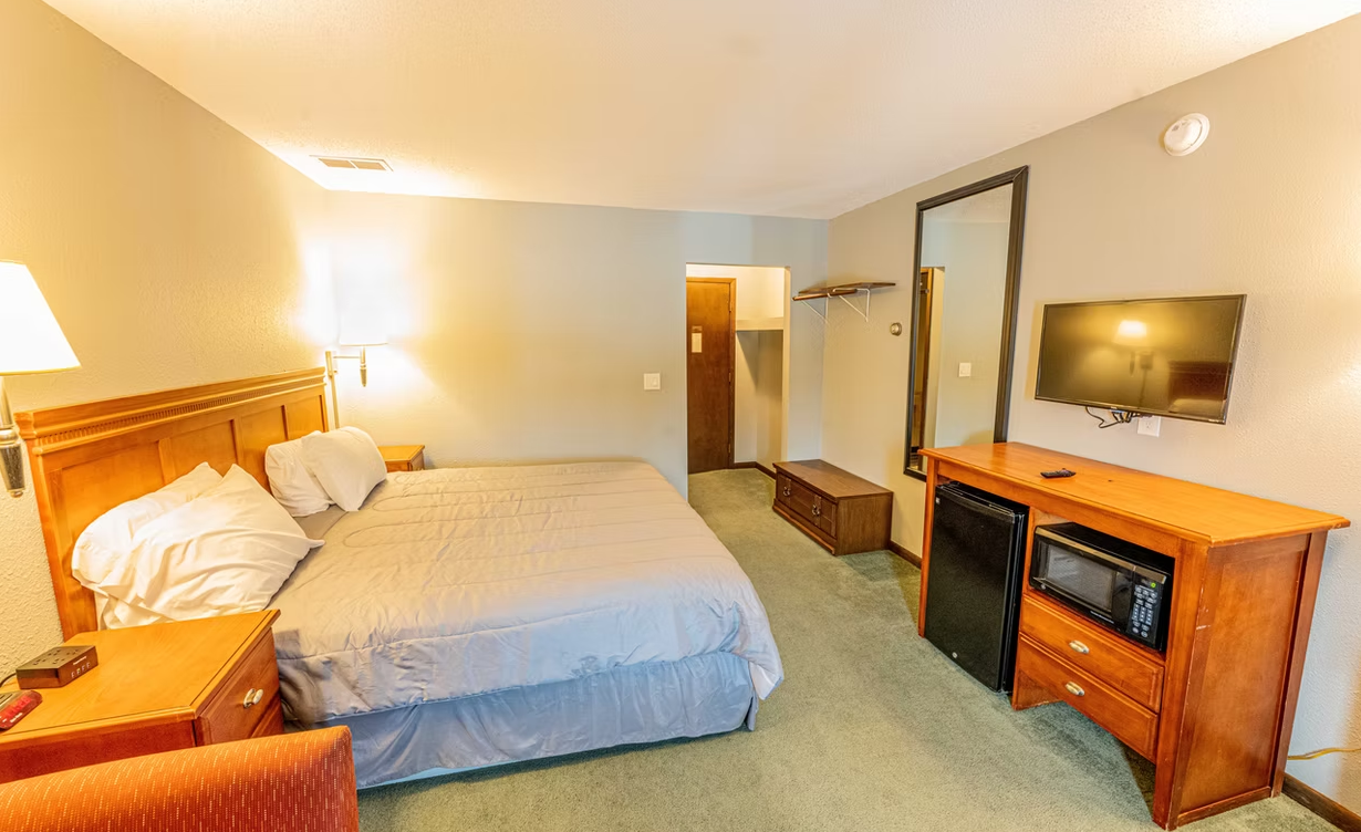 Hotel room with two beds, wall-mounted TV, dresser, and mirrored closet in warm lighting