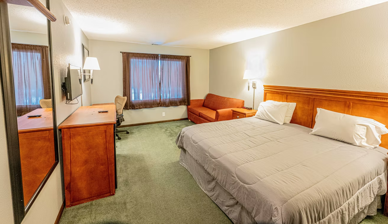 Hotel room with a king bed, orange sofa, wood furniture, and window curtains