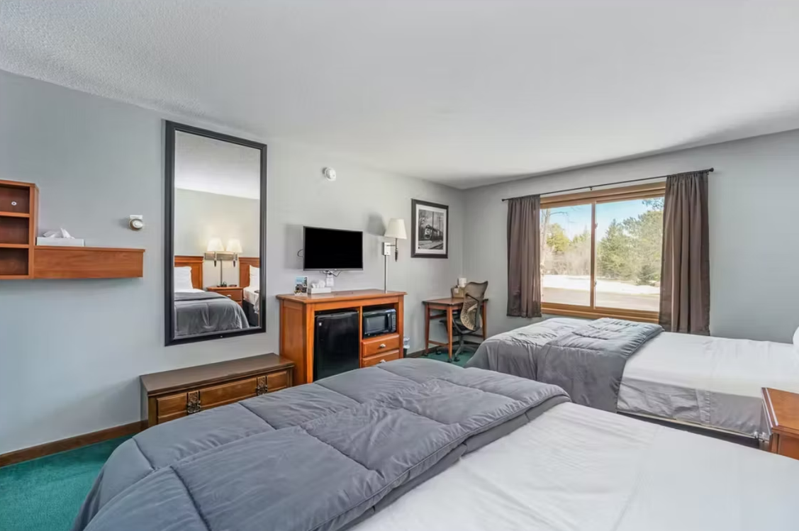 Bright hotel room with two beds, TV, fireplace, and large window with curtains