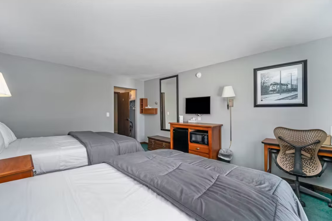 Hotel room with two beds, desk, TV, lamp, and patterned chair in a gray interior