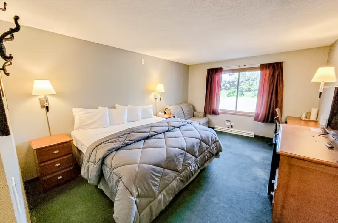 Hotel room with two beds, lamps, a window seat, and green carpet