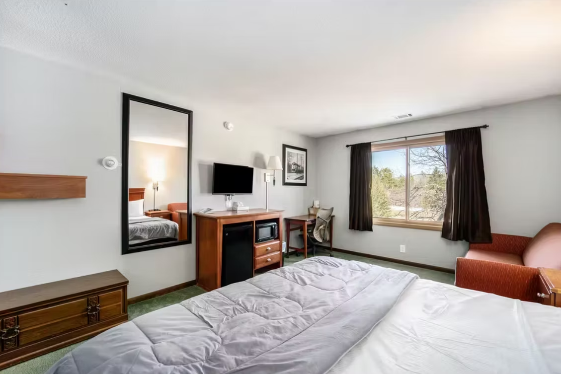 Bright hotel room with a bed, TV, dresser, window, and chair.