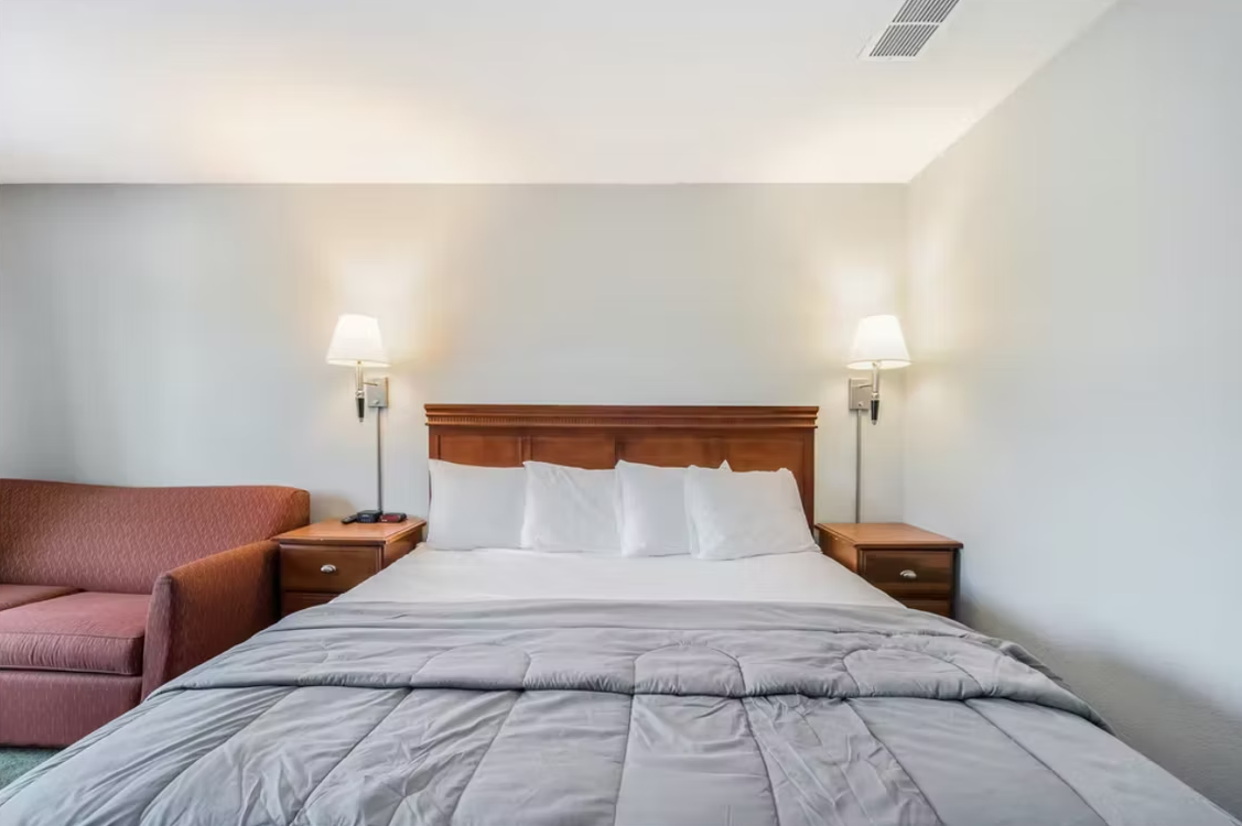 Hotel room with a neatly made bed, two bedside lamps, and a pink sofa on the left