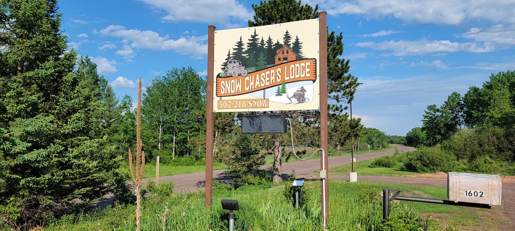 Wooden roadside sign in a green field under a blue sky, reading “Roch Harbor.”