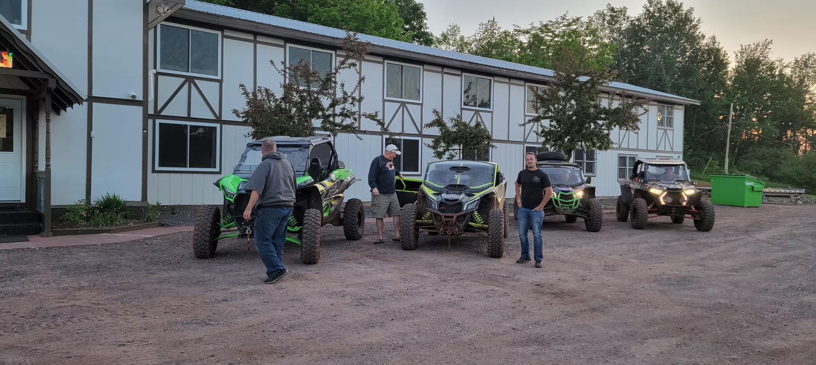 People and off-road vehicles parked outside a white building at dusk