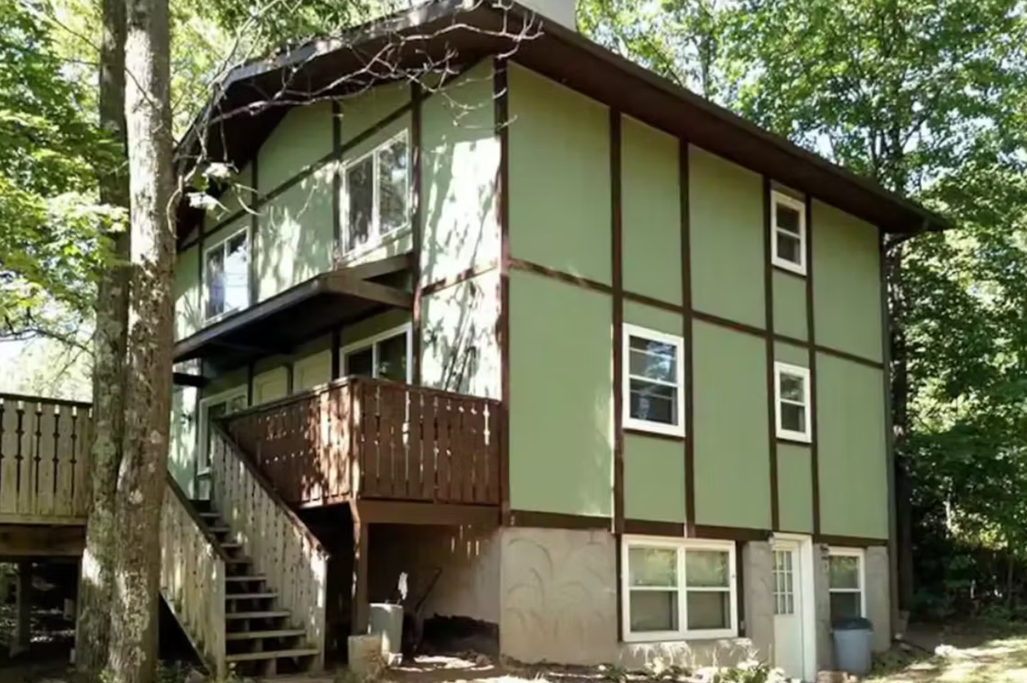 Green two-story house with exterior staircase in a wooded area