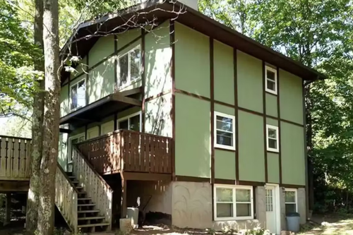 Green two-story house with exterior staircase in a wooded area