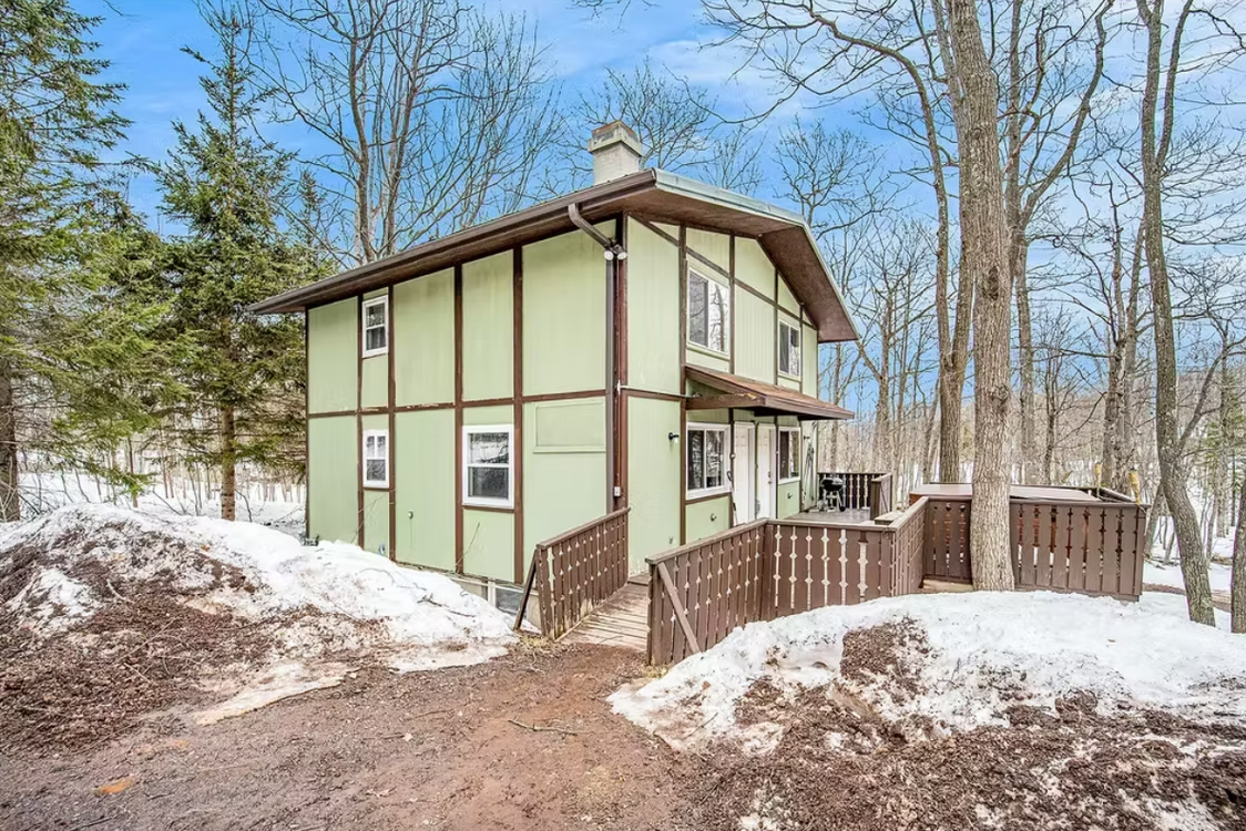 Snowy wooded scene with a small green house and wooden deck on a hillside
