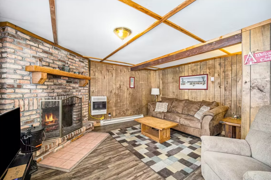 Cozy living room with stone fireplace, tan sectional, patterned rug, and wood-paneled walls