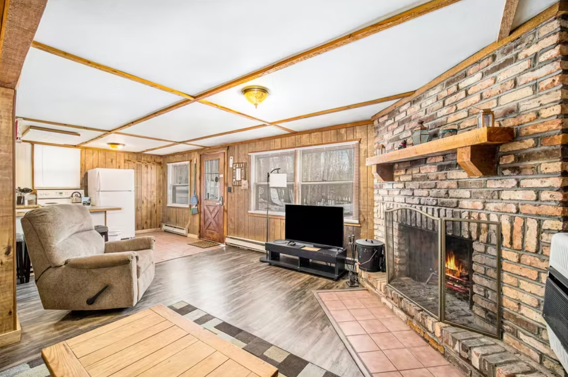 Cozy living room with stone fireplace, wood-paneled walls, recliner, TV, and light wood flooring