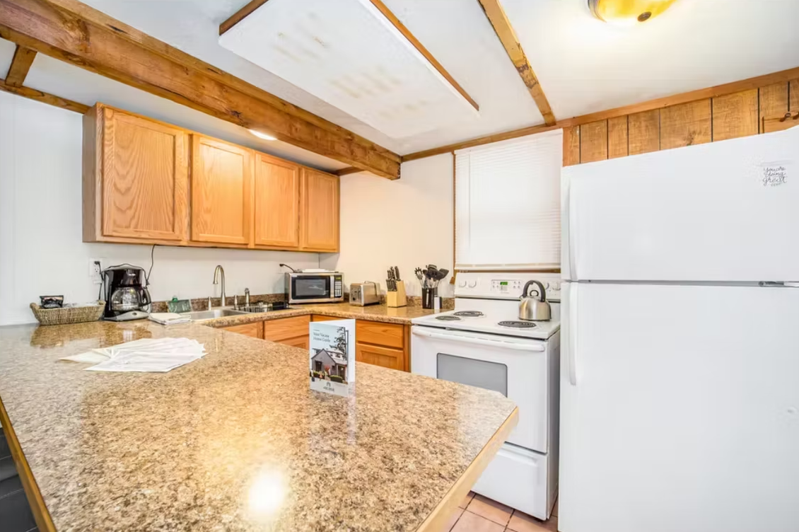 Compact kitchen with granite island, light wood cabinets, white refrigerator, and sink by the window.