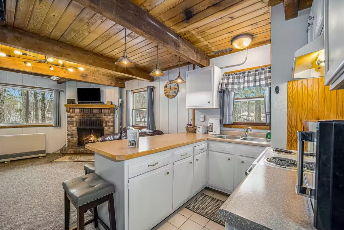 Rustic kitchen with wood ceiling, white cabinets, stone fireplace, and large windows