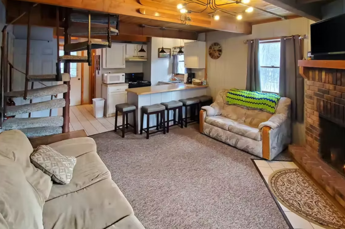 Cozy basement living room with beige sofas, bar counter, stairs, and brick fireplace