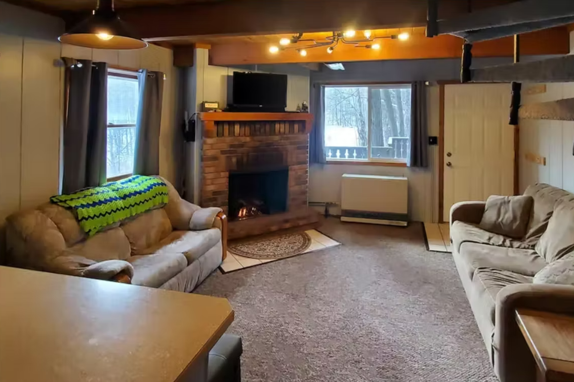 Cozy living room with beige sofas, brick fireplace, windows, and warm ceiling lights