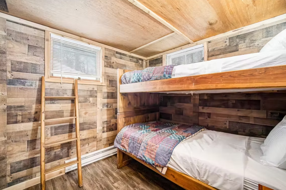 Wood-paneled bunk bedroom with a ladder, patterned bedding, and a small window