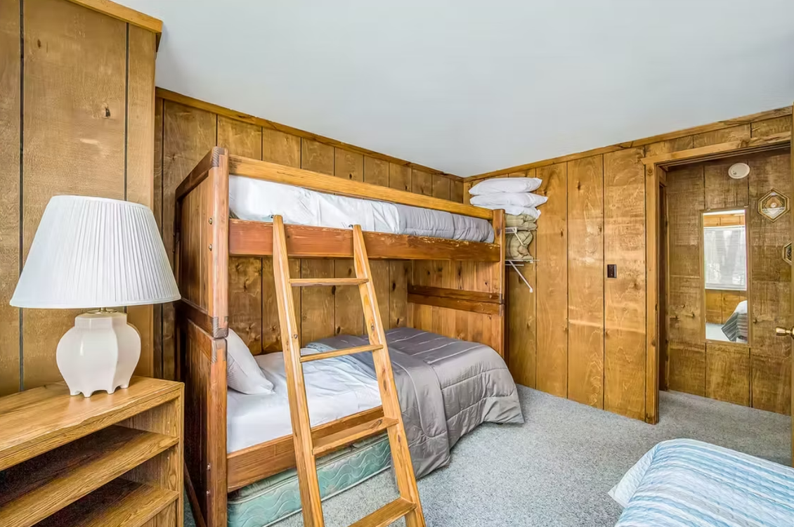 Wood-paneled bunk bedroom with two beds, a lamp, and a door to the right.