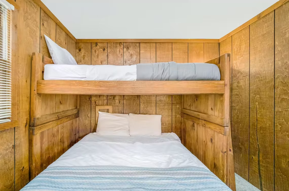 Wood-paneled bunk bedroom with two neatly made beds and white bedding