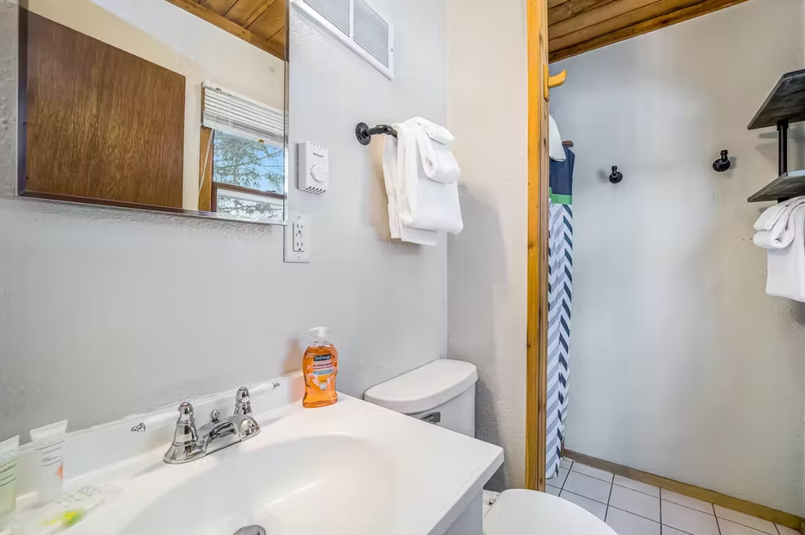 Small bathroom with a sink, toilet, mirror, and shower curtain; towel hanging on the wall.