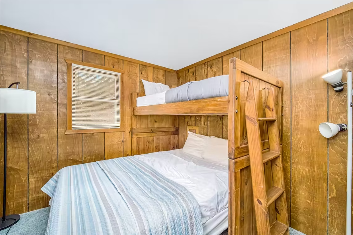 Wood-paneled bunk room with two wooden bunk beds, white bedding, and a wall lamp