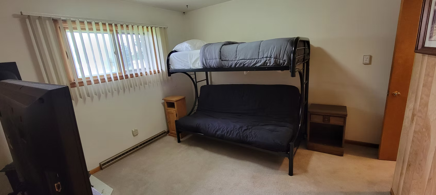 Small bedroom with bunk bed, window, nightstand, and dresser on carpet.