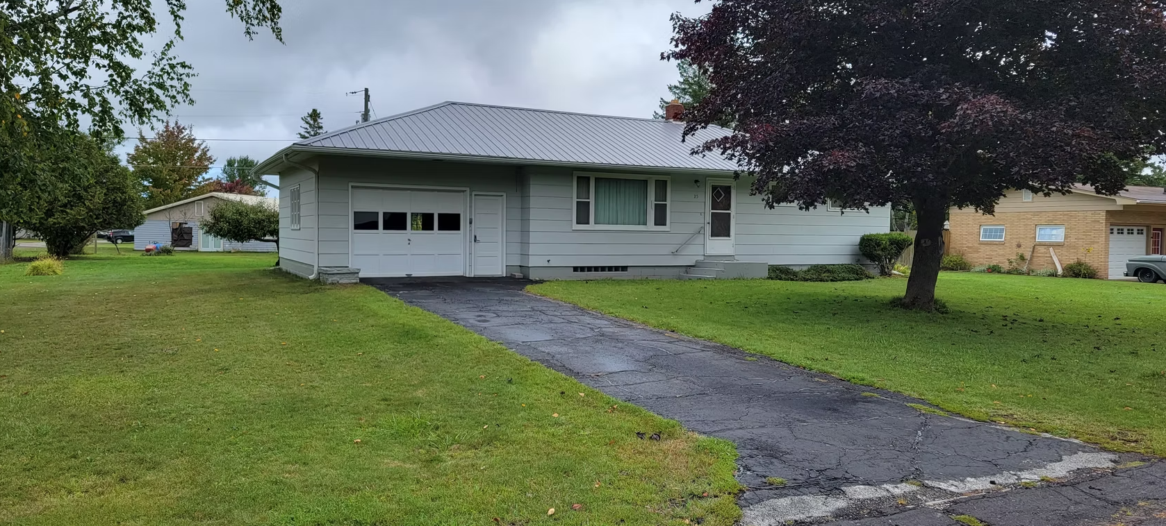 Single-story white house with attached garage, dark driveway, and green lawn on a cloudy day