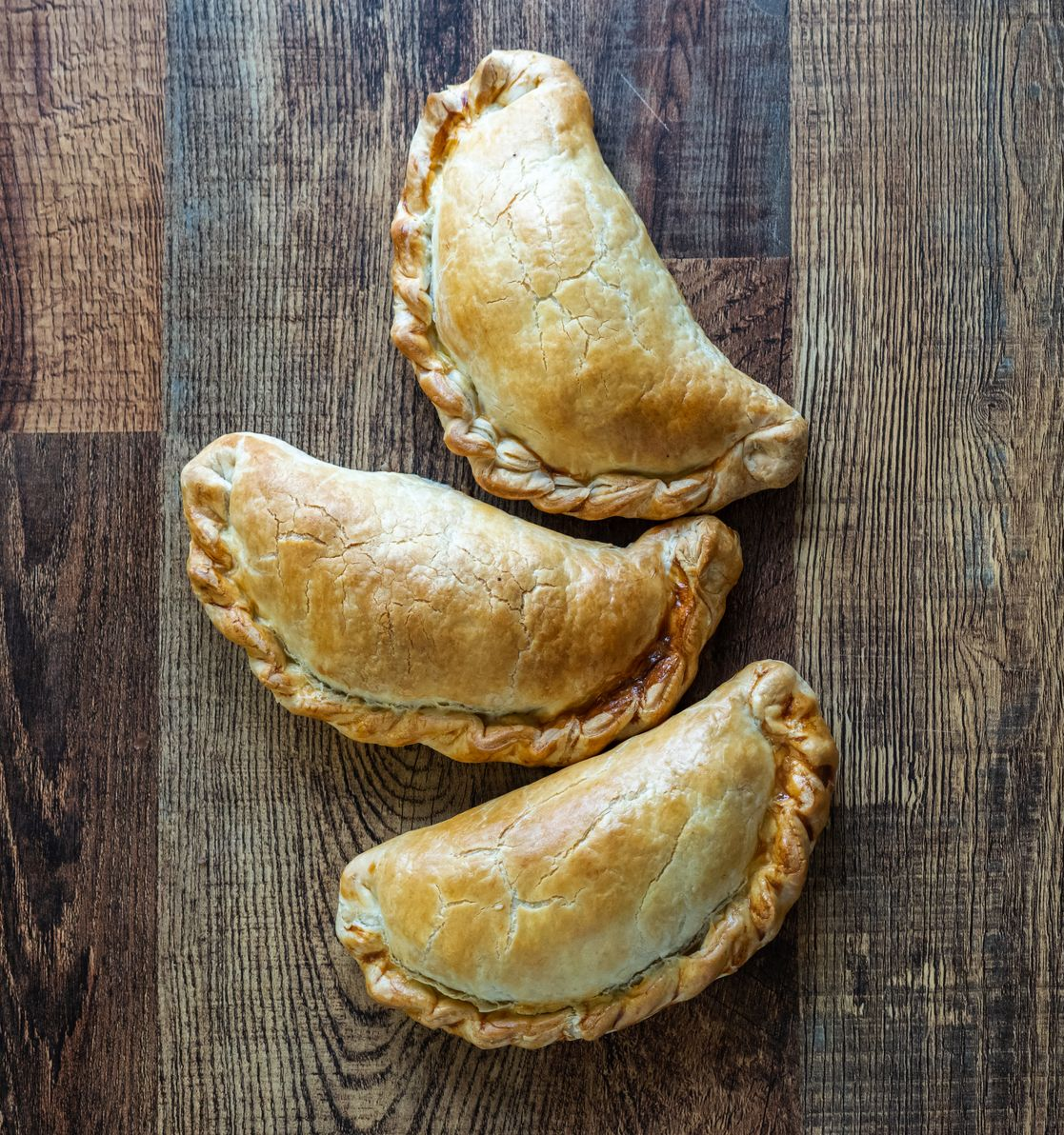 Three golden baked pastries on a wooden table.