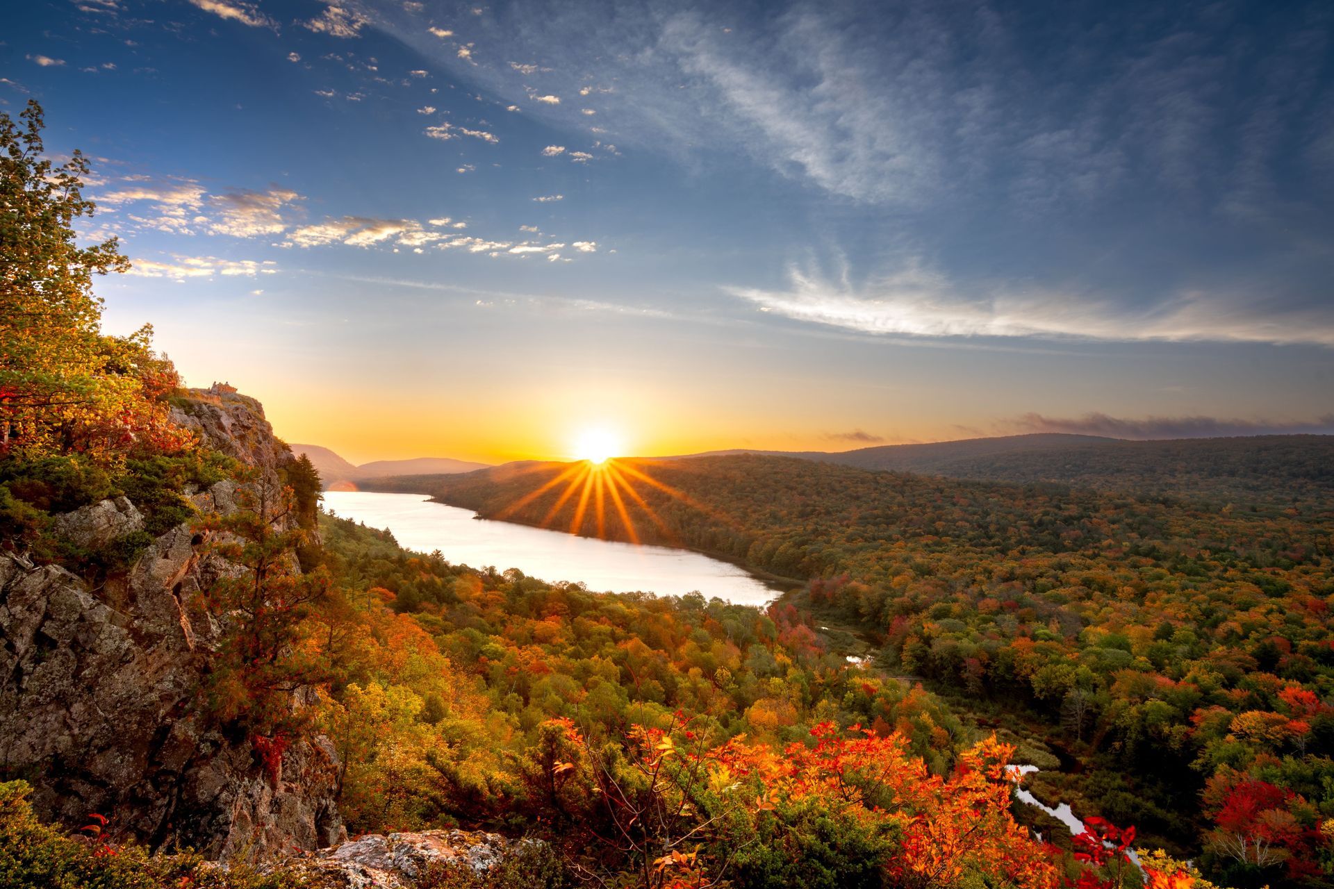 Sunrise over a forested valley with a winding lake, autumn foliage, and dramatic clouds