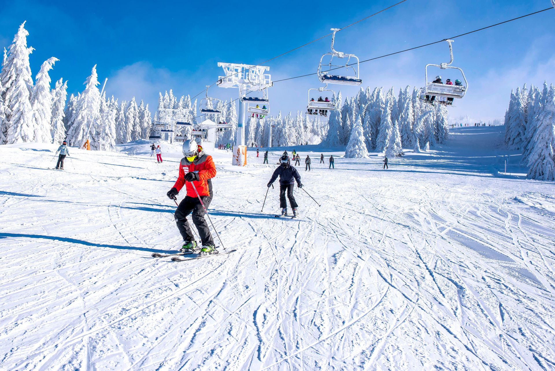 Skiers descending a snowy slope beneath chairlifts in a bright winter mountain resort