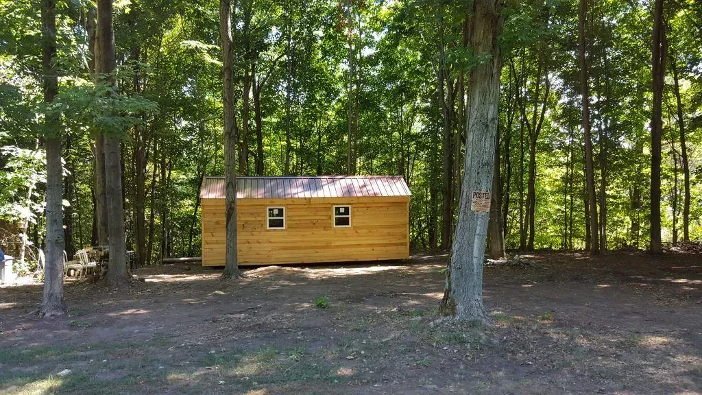 A small, wooden cabin with a metal roof, surrounded by trees.