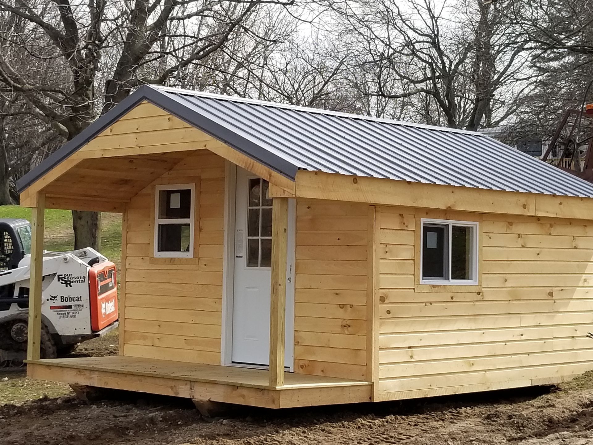 Wooden shed with brown metal roof, green grass, and two hinged doors.