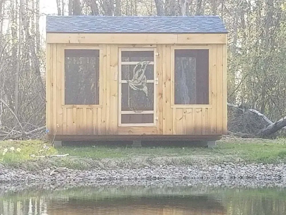 Wooden cabin with windows and a screen door, near a river.