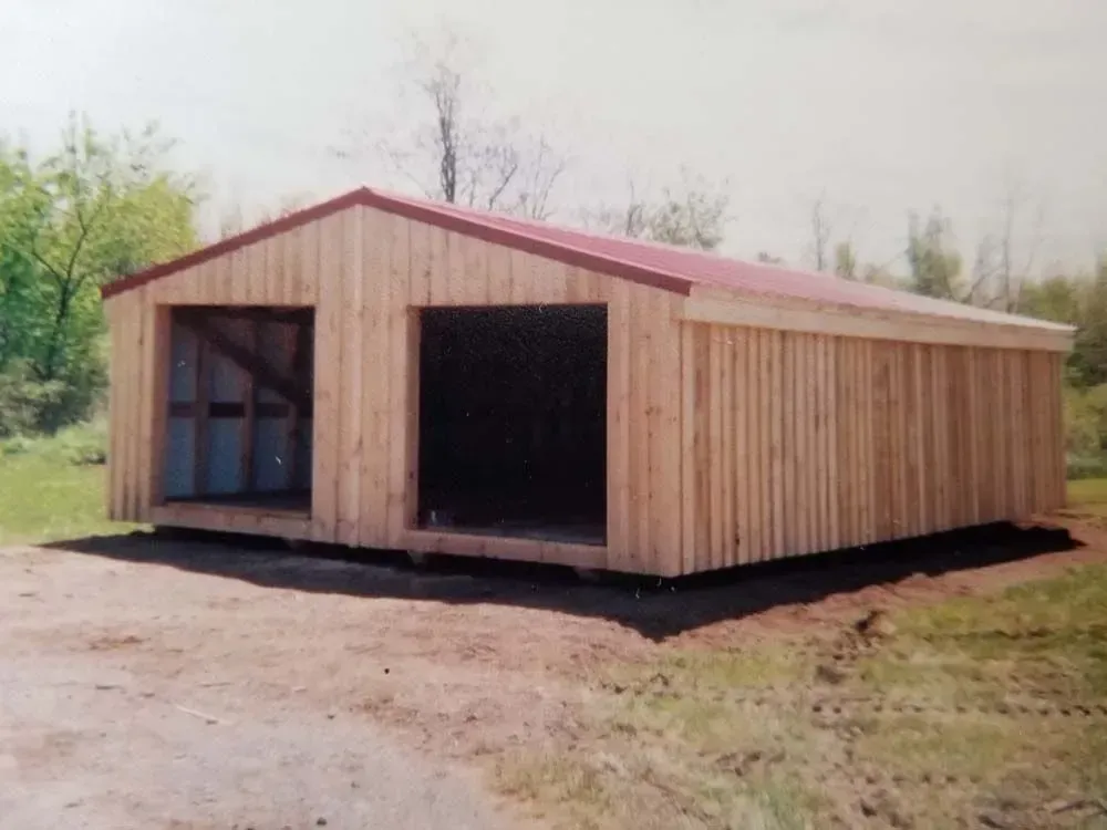 Two-bay wooden garage with a red roof, in a rural setting.