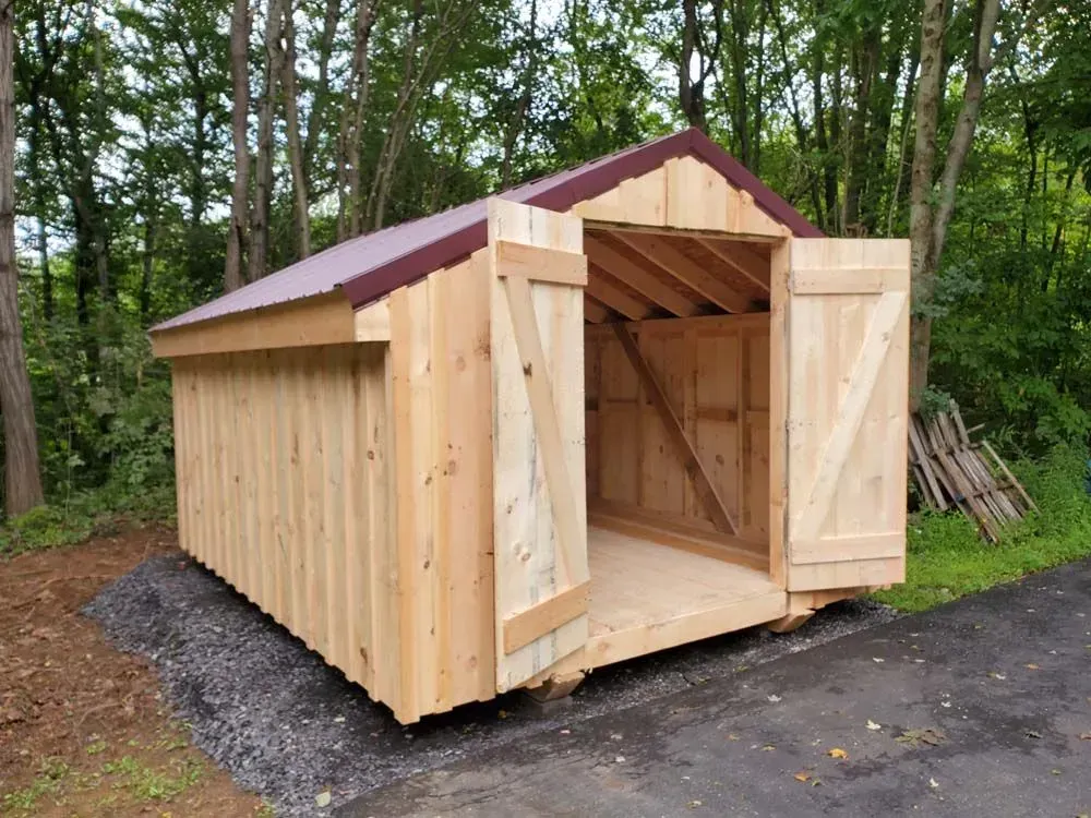 Wooden shed with open doors, set on gravel near trees.