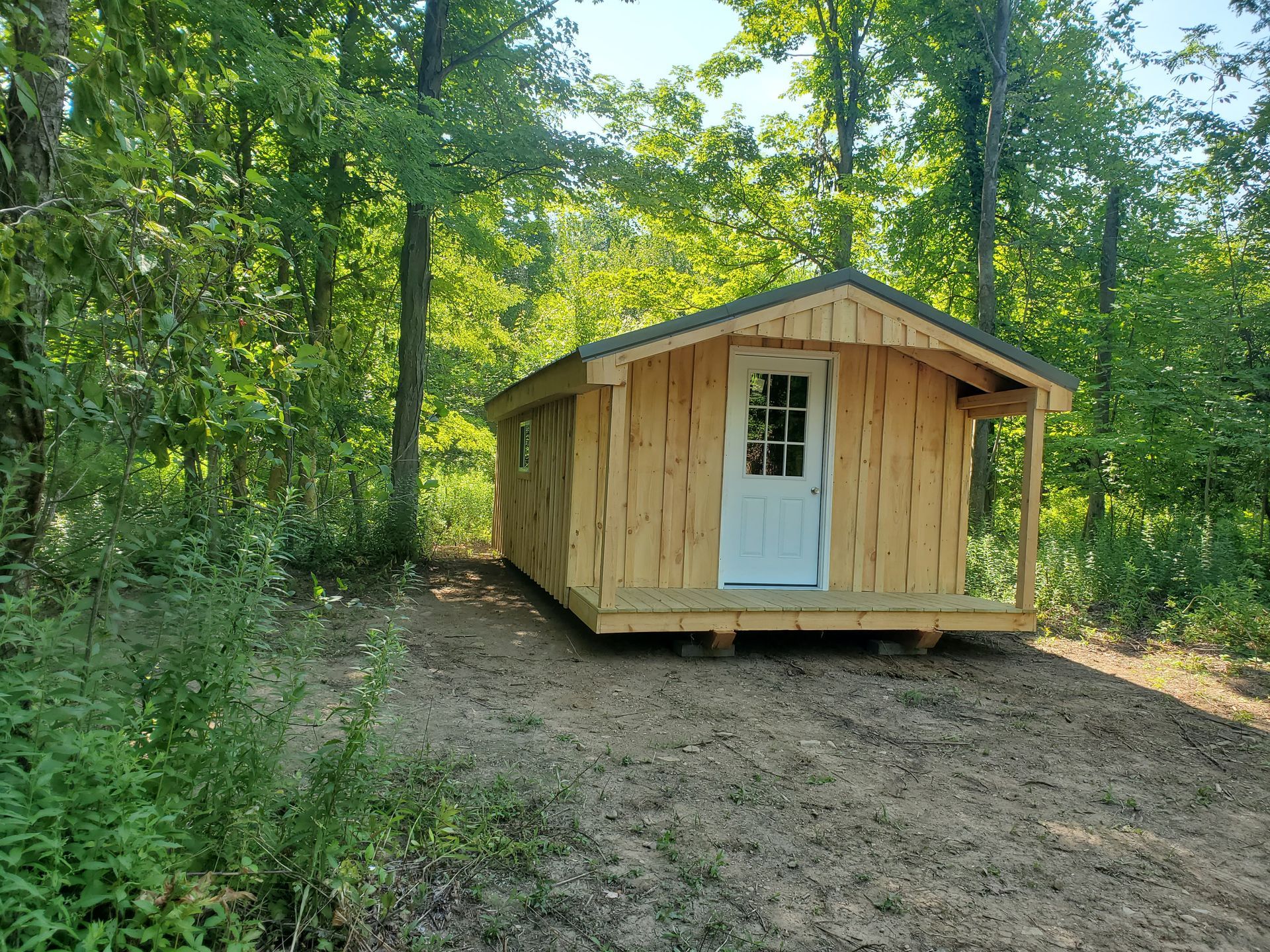 Wooden shed with brown metal roof in a grassy field.