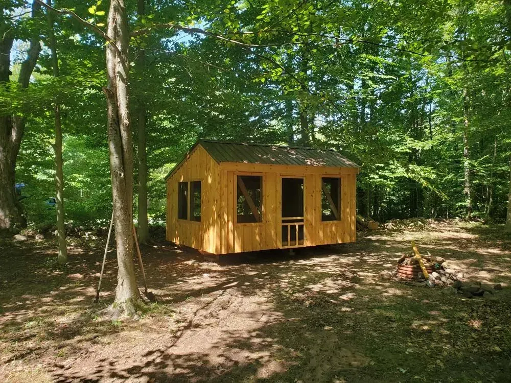 Wooden cabin in a forest, with sunlight filtering through the trees.