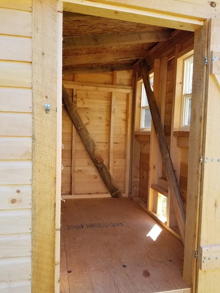 Wooden shed interior with diagonal supports, door frame, windows, and unfinished floor.