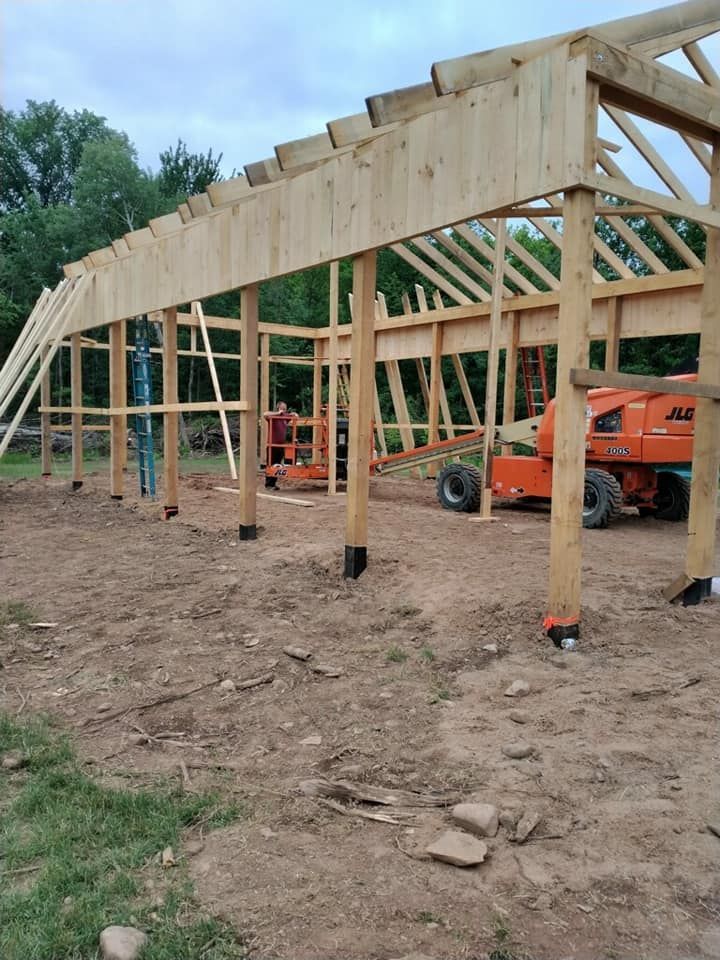 Construction of a wooden barn frame; orange lift equipment in the center; building on a dirt ground.