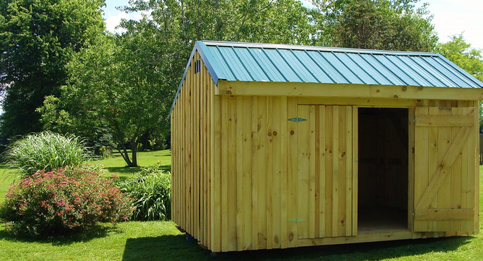 Wooden shed with green roof and open doorway in a grassy yard.