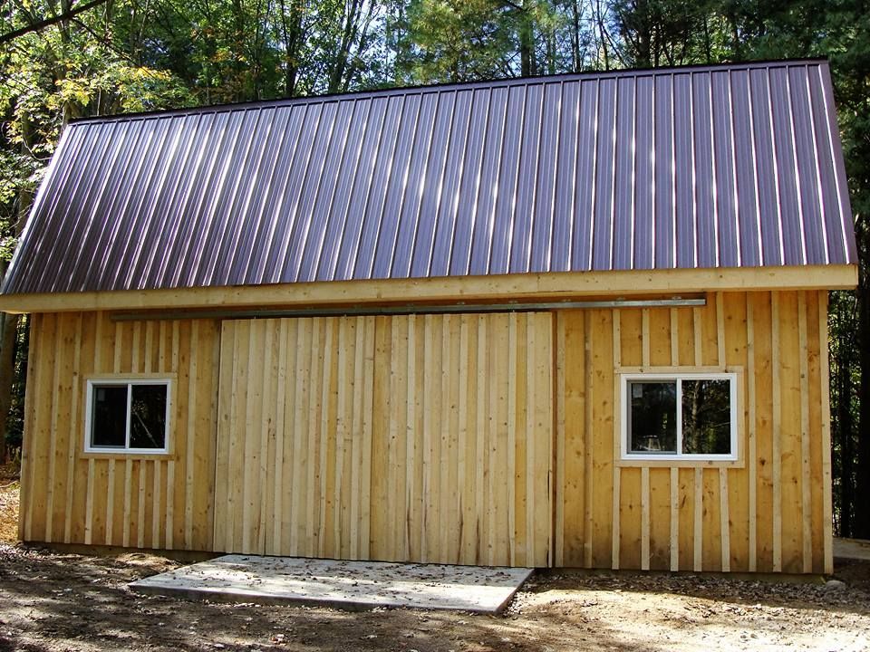 Wooden shed with a brown metal roof, a large sliding door, and two windows.