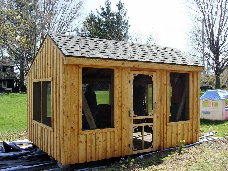 Wooden shed with windows and screen door, on a grassy lawn.