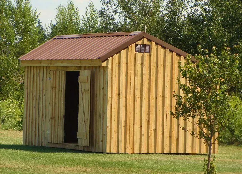 Wooden shed with brown metal roof and open door on a green lawn.
