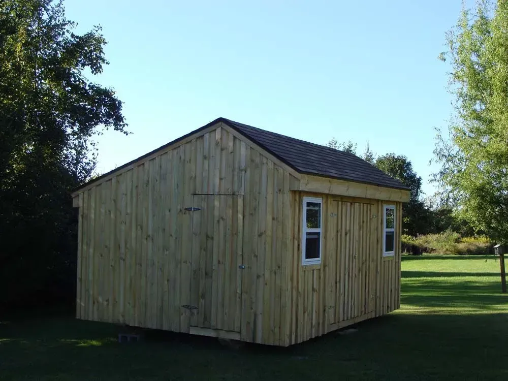 Wooden shed with a black roof, two windows, and a door, set on a green lawn under a blue sky.
