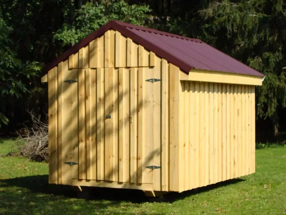 Wooden shed with a burgundy metal roof in a grassy area.