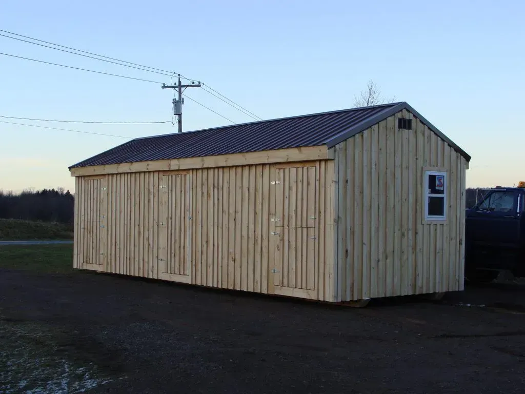 Wooden shed with dark roof and small window, set on asphalt with power lines in background.