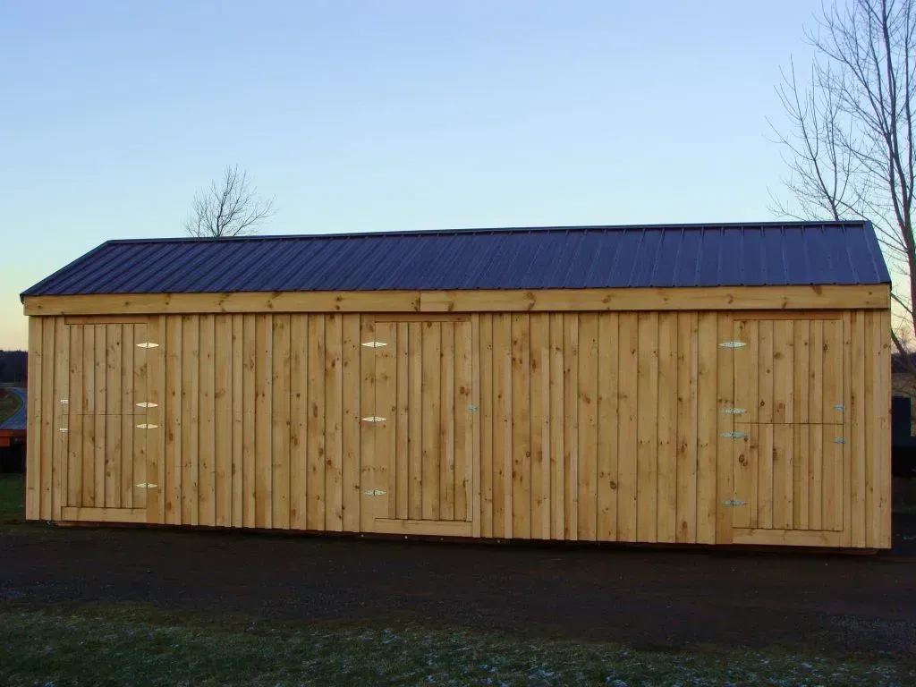 Wooden shed with a dark metal roof, several doors, in an outdoor setting.