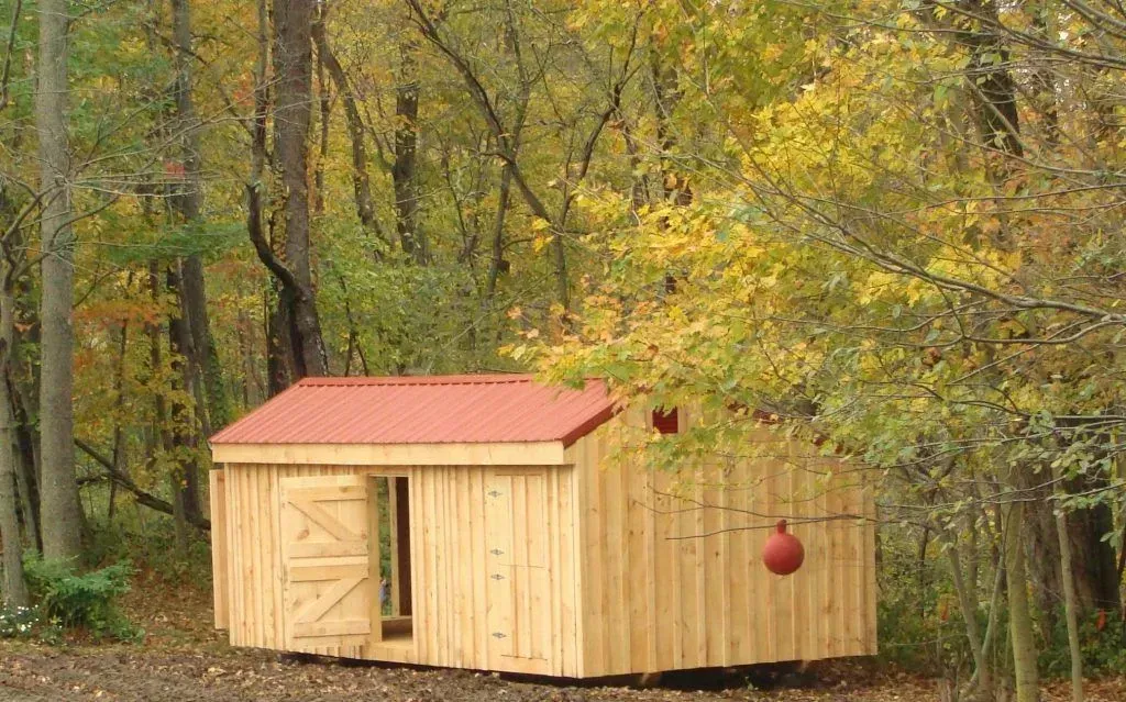 Wooden shed with red roof in a forest. Open doorway, two doors. A red ball hangs on the side.