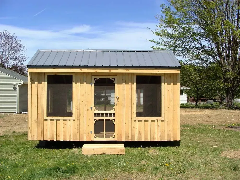Small wooden shed with metal roof and screen door in a grassy yard.