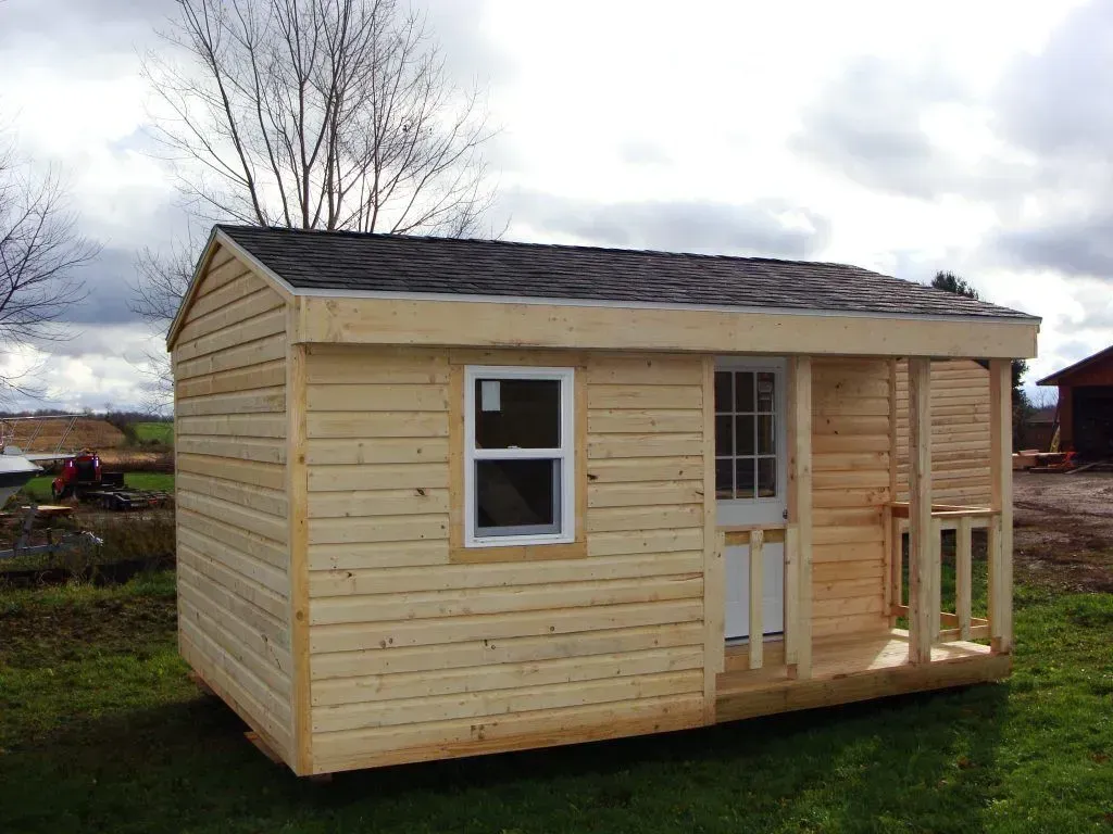 Small unfinished wooden shed with a window, door, and small porch on a grassy field.