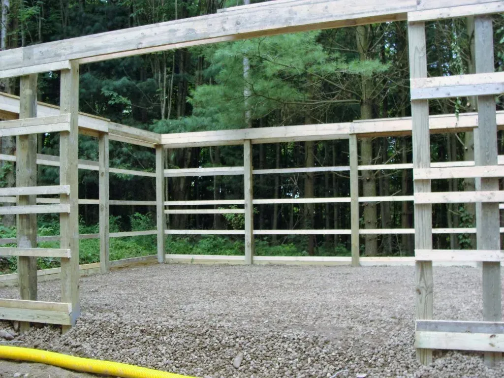 Wooden structure under construction with gravel floor, surrounded by trees.